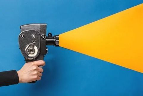 Hand holding a vintage cine camera that projects a yellow beam across a blue background