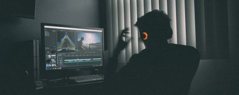 Person wearing headphones editing video on a desktop monitor in a dimly lit room